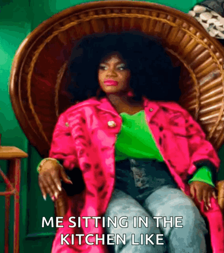 A Woman In A Pink Jacket And Green Shirt Is Sitting In A Wicker Chair With The Caption Me Sitting In The Kitchen Like GIF