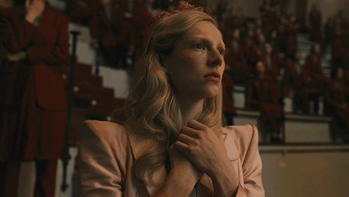 A Woman In A Pink Jacket Has Her Hands Folded In Front Of A Crowd GIF