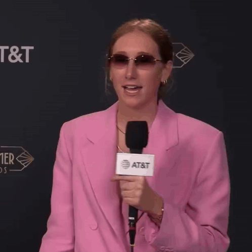 a woman in a pink jacket holds a microphone that says at & t on it