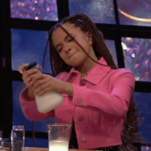 A Woman In A Pink Jacket Is Pouring Milk Into A Cup GIF