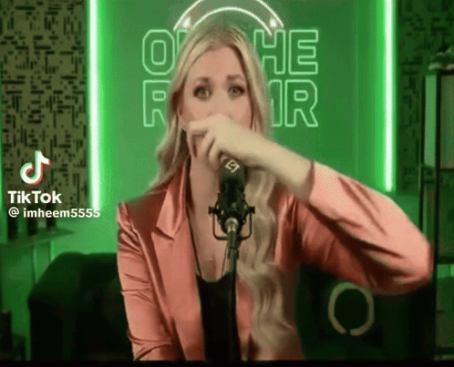 A Woman In A Pink Jacket Is Singing Into A Microphone In Front Of A Neon Sign That Says Othe Fair GIF