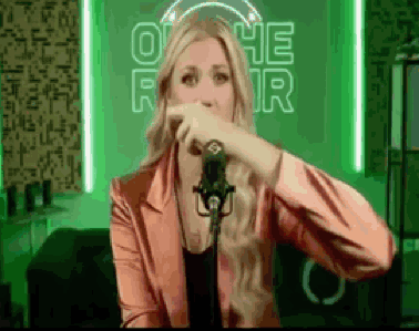 A Woman In A Pink Jacket Is Singing Into A Microphone In Front Of A Neon Sign That Says Othe For GIF