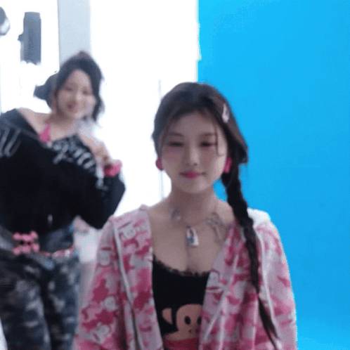 A Woman In A Pink Jacket Is Standing In Front Of A Blue Background GIF