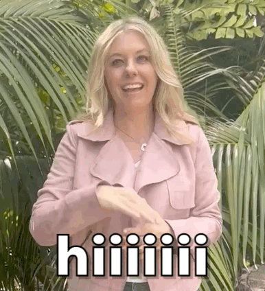 A Woman In A Pink Jacket Is Standing In Front Of Palm Trees And Making A Funny Face . GIF