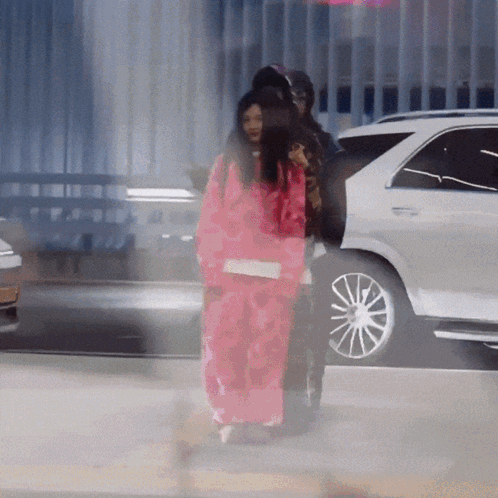 A Woman In A Pink Jacket Is Walking In Front Of A Car GIF