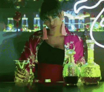 A Woman In A Pink Kimono Stands Behind A Bar With Bottles Of Alcohol GIF