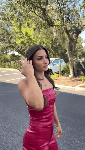 a woman in a pink leather dress is standing on the side of the road .