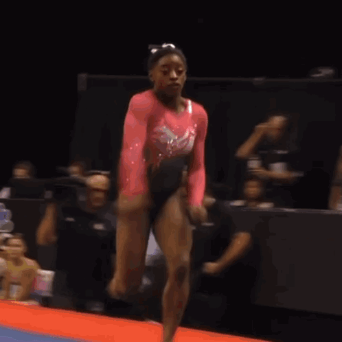 A Woman In A Pink Leotard Is Doing A Trick In Front Of A Sign That Says 215 GIF