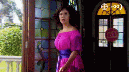 A Woman In A Pink Off The Shoulder Dress Stands In Front Of A Stained Glass Window . GIF