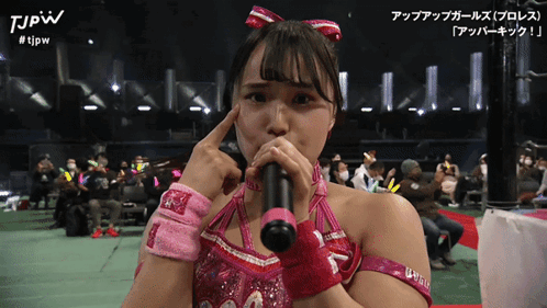 a woman in a pink outfit is holding a microphone and the words tjpw are on the bottom right