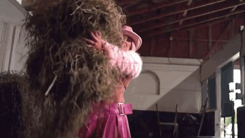 A Woman In A Pink Outfit Is Holding A Pile Of Hay . GIF