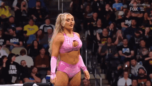 A Woman In A Pink Outfit Is Standing In Front Of A Crowd In A Wrestling Ring . GIF