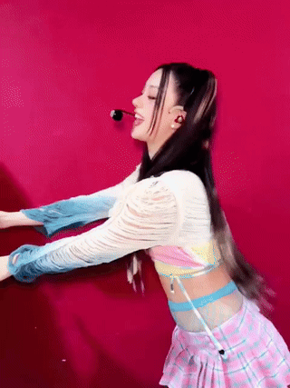 A Woman In A Pink Plaid Skirt Is Dancing In Front Of A Red Background GIF