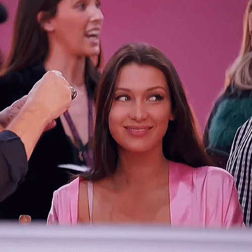 A Woman In A Pink Robe Is Smiling While Sitting In A Crowd Of People . GIF