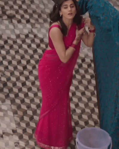 A Woman In A Pink Saree Is Standing Next To A Bucket On A Tiled Floor GIF