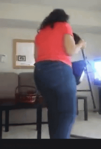 A Woman In A Pink Shirt And Blue Jeans Is Standing In Front Of A Mirror GIF
