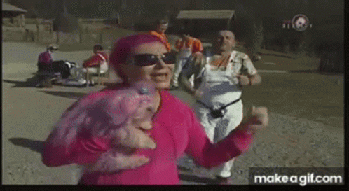 A Woman In A Pink Shirt Is Dancing In A Park With Other People . GIF