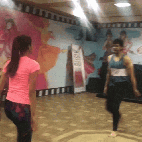 A Woman In A Pink Shirt Is Dancing In Front Of A Sign That Says ' A ' On It GIF