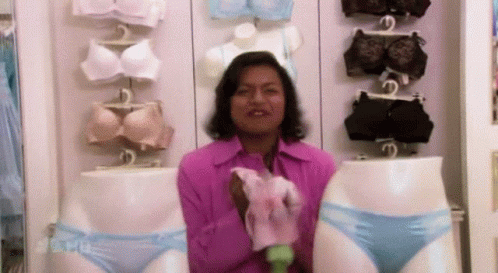 A Woman In A Pink Shirt Is Holding A Pair Of Blue Underwear In Front Of Mannequins . GIF