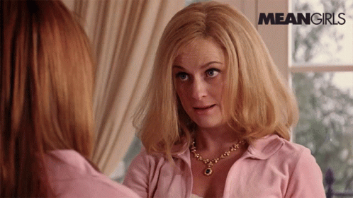 A Woman In A Pink Shirt Is Looking At Another Woman In Front Of A Window With Meangirls Written On The Bottom GIF