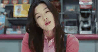 A Woman In A Pink Shirt Is Sitting At A Counter In A Store And Making A Funny Face . GIF