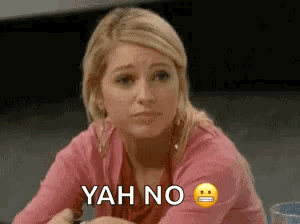 A Woman In A Pink Shirt Is Sitting At A Table With A Smiley Face And The Words `` Yah No '' . GIF