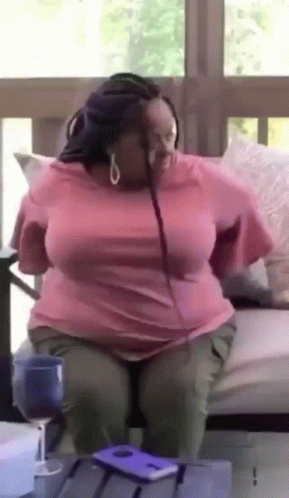 A Woman In A Pink Shirt Is Sitting On A Couch With Her Legs Crossed . GIF