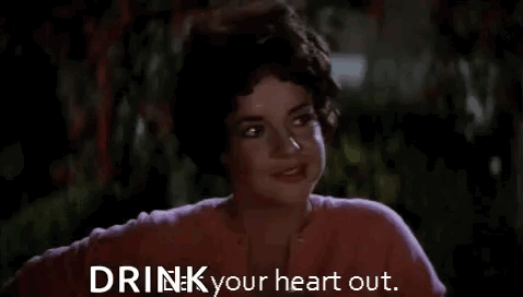 A Woman In A Pink Shirt Is Smiling And Says `` Drink Your Heart Out . '' GIF
