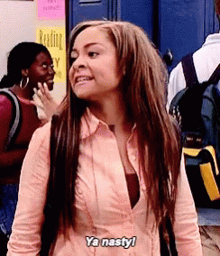 A Woman In A Pink Shirt Is Standing In Front Of A Blue Door . GIF