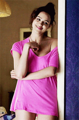 A Woman In A Pink Shirt Is Standing In Front Of A Blue Wall GIF