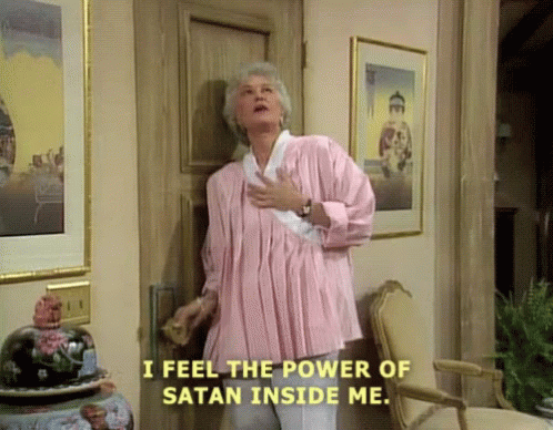 A Woman In A Pink Shirt Is Standing In Front Of A Door Saying I Feel The Power Of Satan Inside Me . GIF
