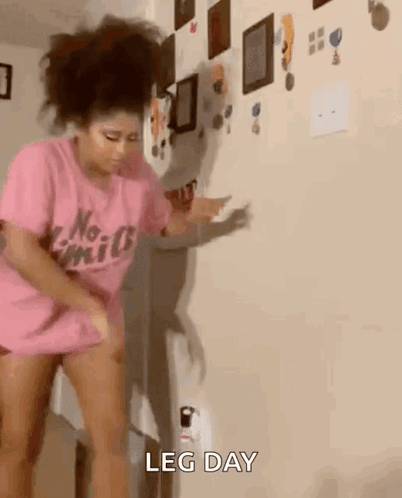 A Woman In A Pink Shirt Is Standing In Front Of A Wall And Dancing . GIF