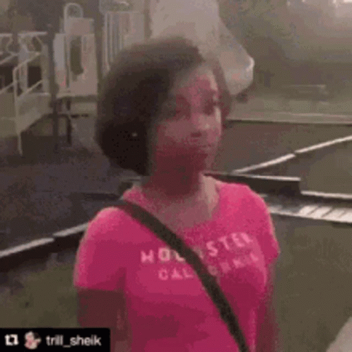 A Woman In A Pink Shirt Is Standing On A Sidewalk With A Bicycle In The Background And Says Do You Wanna Fight ? GIF