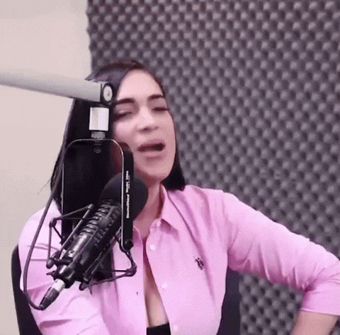 A Woman In A Pink Shirt Is Talking Into A Microphone GIF