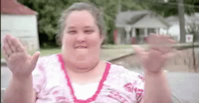 A Woman In A Pink Shirt Is Waving Her Hands In The Air . GIF
