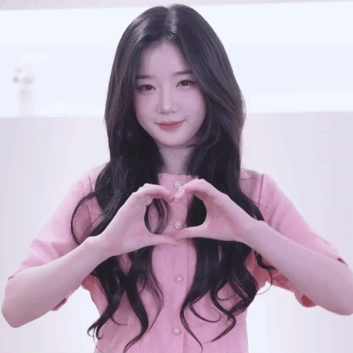 A Woman In A Pink Shirt Making A Heart Shape With Her Hands GIF
