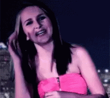 A Woman In A Pink Strapless Top Is Smiling And Holding Her Hair GIF