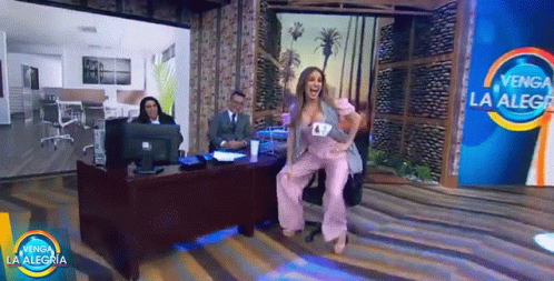 A Woman In A Pink Suit Is Dancing In Front Of A Sign That Says " Venga La Alegria " GIF