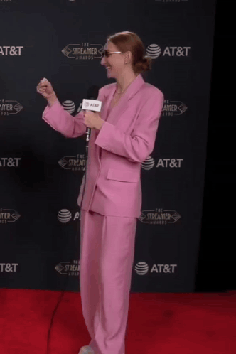 a woman in a pink suit is holding a microphone in front of an at & t wall