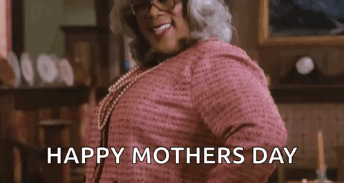 A Woman In A Pink Sweater And Glasses Is Standing In A Living Room And Smiling . GIF