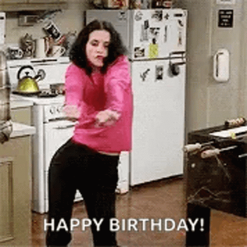 A Woman In A Pink Sweater Is Dancing In A Kitchen With The Words `` Happy Birthday '' Written Below Her . GIF