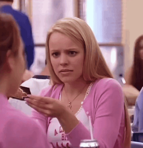 A Woman In A Pink Sweater Is Holding A Piece Of Cake In Her Hand And Talking To Another Woman . GIF
