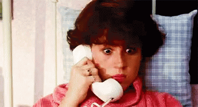 Woman In Pink Sweater Lying In Bed Talking On Phone GIF