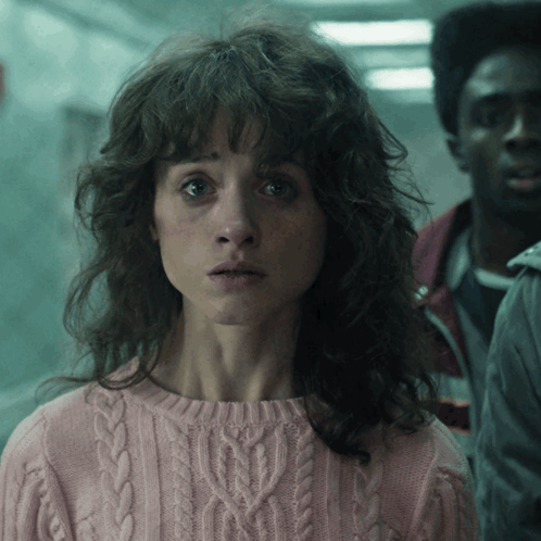 A Woman In A Pink Sweater Is Looking At The Camera GIF