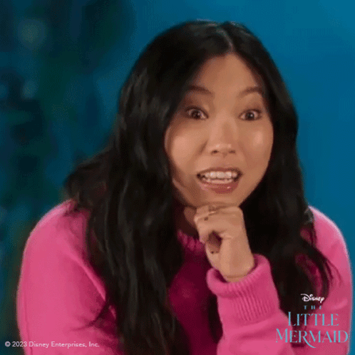 A Woman In A Pink Sweater Is Making A Surprised Face While Holding Her Hands To Her Chin . GIF