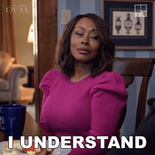 A Woman In A Pink Sweater Is Sitting At A Table And Says " I Understand " GIF