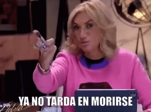 a woman in a pink sweater is sitting in front of a laptop and holding a cell phone in her hand .