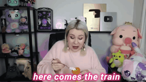 a woman in a pink sweater is sitting in front of stuffed animals and says " here comes the train "