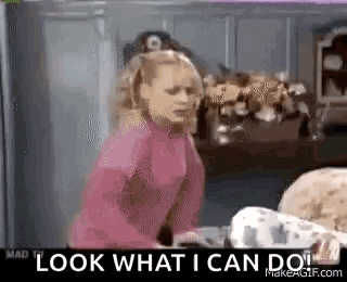 A Woman In A Pink Sweater Is Standing In A Kitchen And Looking At A Baby . GIF