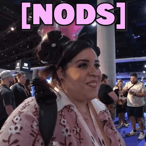 A Woman In A Pink Sweater Stands In Front Of A Sign That Says ' Nods ' GIF